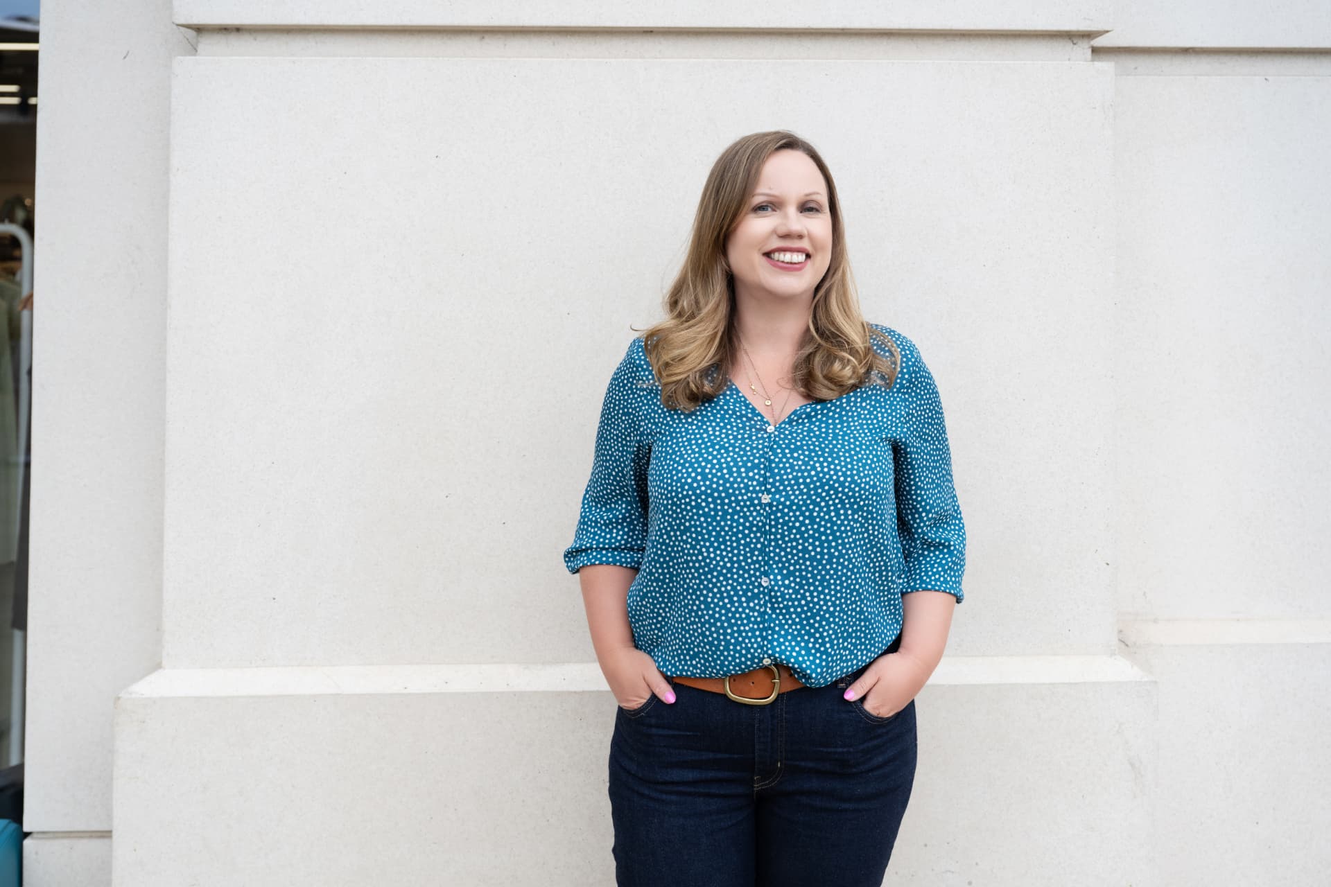 Jo leaning against a pale stone wall, relaxed and smiling